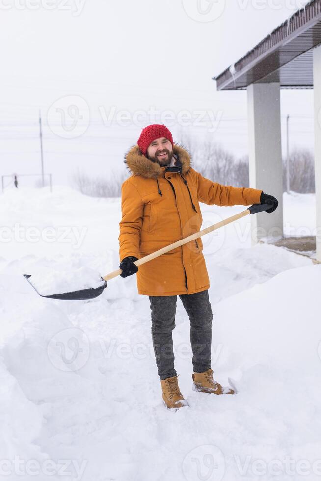 Young man clearing snow in his backyard village house with shovel. Remove snow from the sidewalk. photo