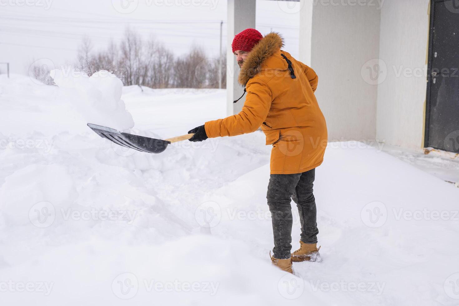 A man cleans and clears the snow in front of the house on frosty day. Cleaning the street from snow on a winter day. Snowfall and severe snowstorm in winter. photo