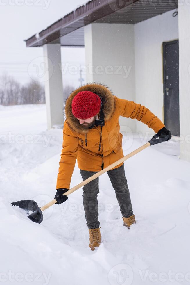 Young man clearing snow in his backyard village house with shovel. Remove snow from the sidewalk. photo
