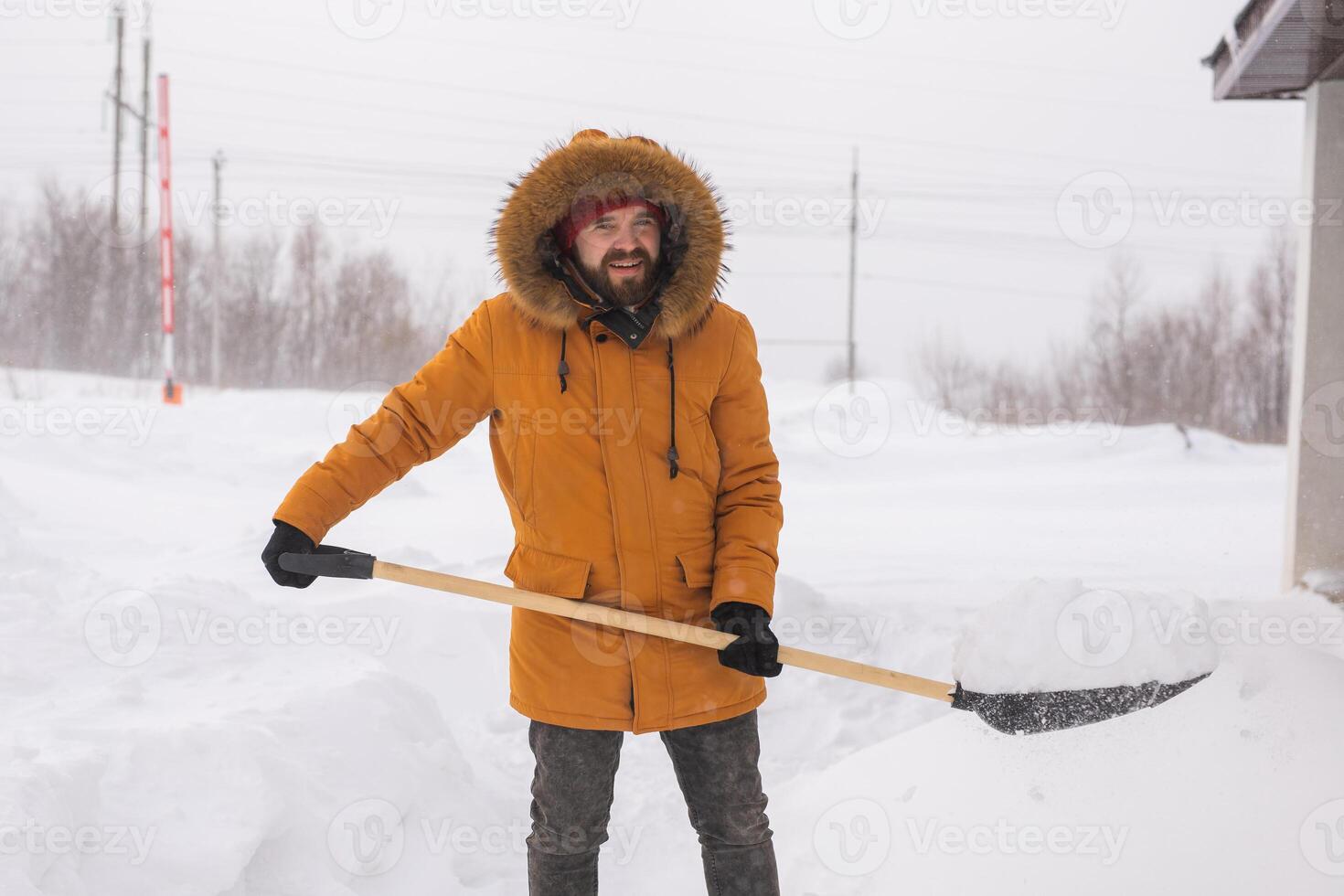 Young man clearing snow in his backyard village house with shovel. Remove snow from the sidewalk. photo