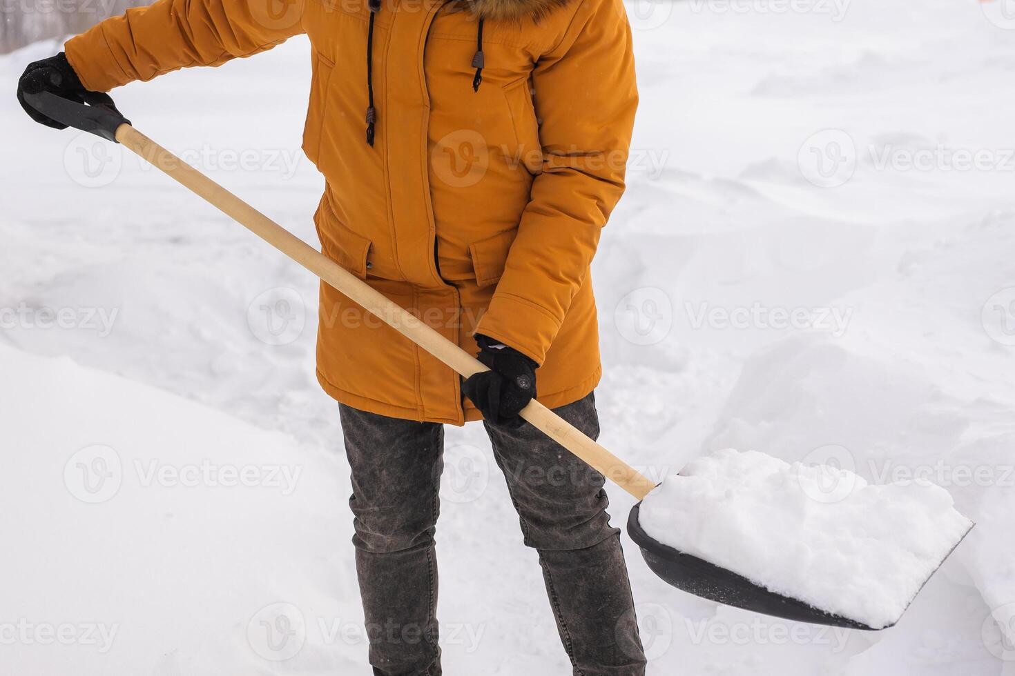Close-up man cleans and clears the snow in front of the house on frosty day. Cleaning the street from snow on a winter day. Snowfall and severe snowstorm in winter. photo