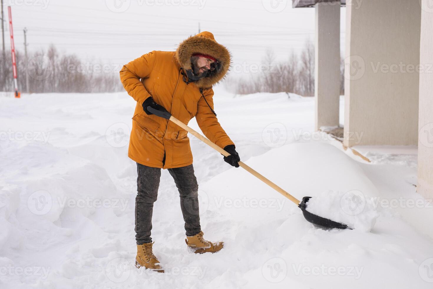 Young man clearing snow in his backyard village house with shovel. Remove snow from the sidewalk. photo