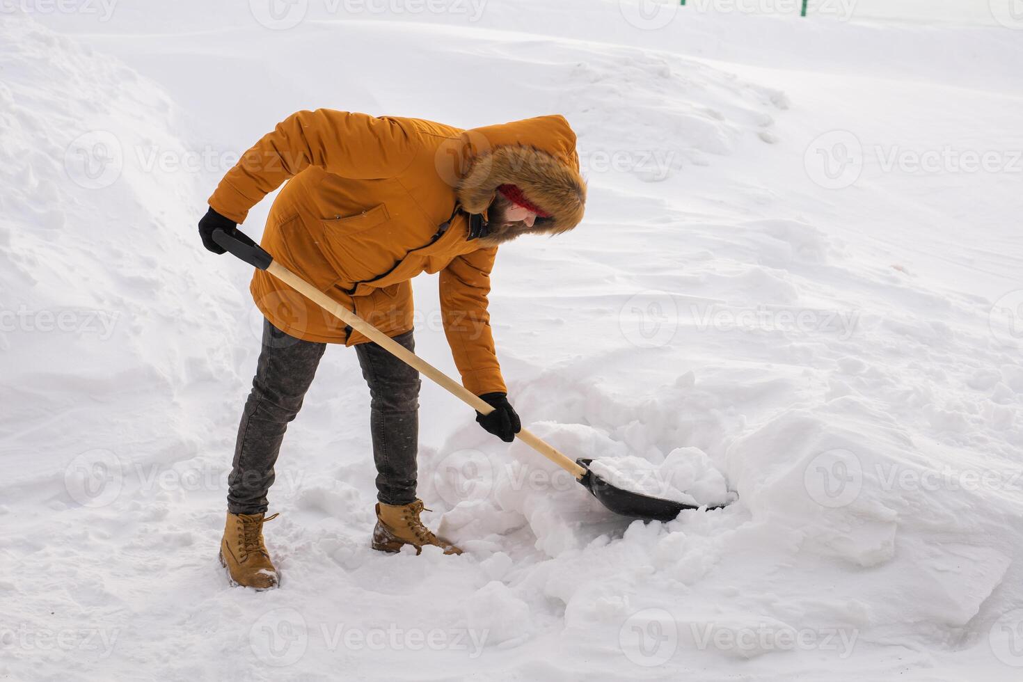 Young man clearing snow in his backyard village house with shovel. Remove snow from the sidewalk. photo
