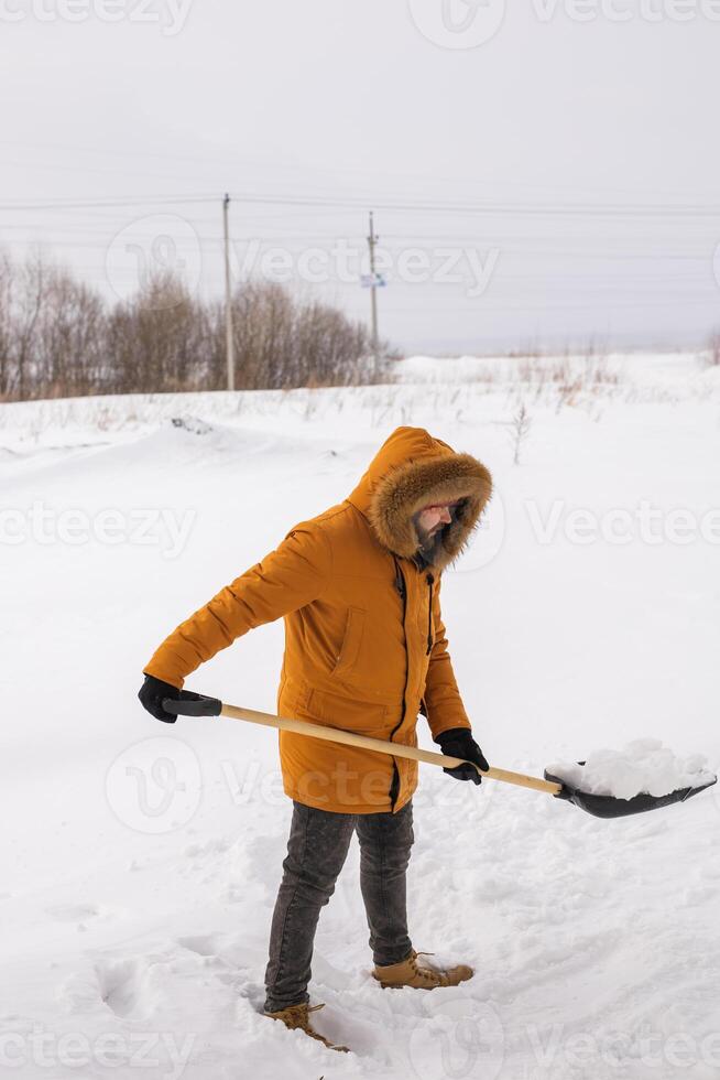 A man cleans and clears the snow in front of the house on frosty day. Cleaning the street from snow on a winter day. Snowfall and severe snowstorm in winter. photo