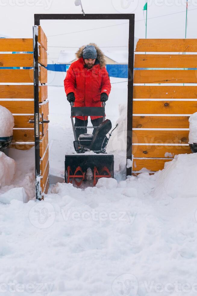 Closeup of red snow blower in action. Senior mature man outdoor in front of house using snowblower machine for removing snow on yard. Snow thrower in winter outside home. Young worker guy blowing snow photo