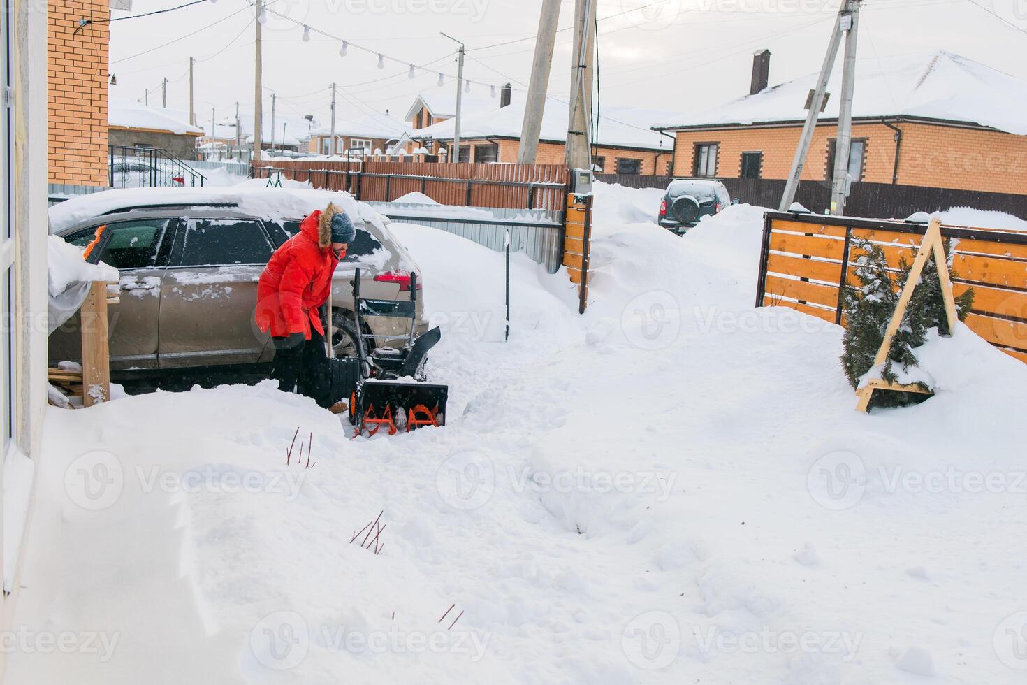 Red snow blower in action. Man outdoor in front of house using snowblower machine for removing snow on yard. Snow thrower in winter outside home. Young worker guy blowing snow photo
