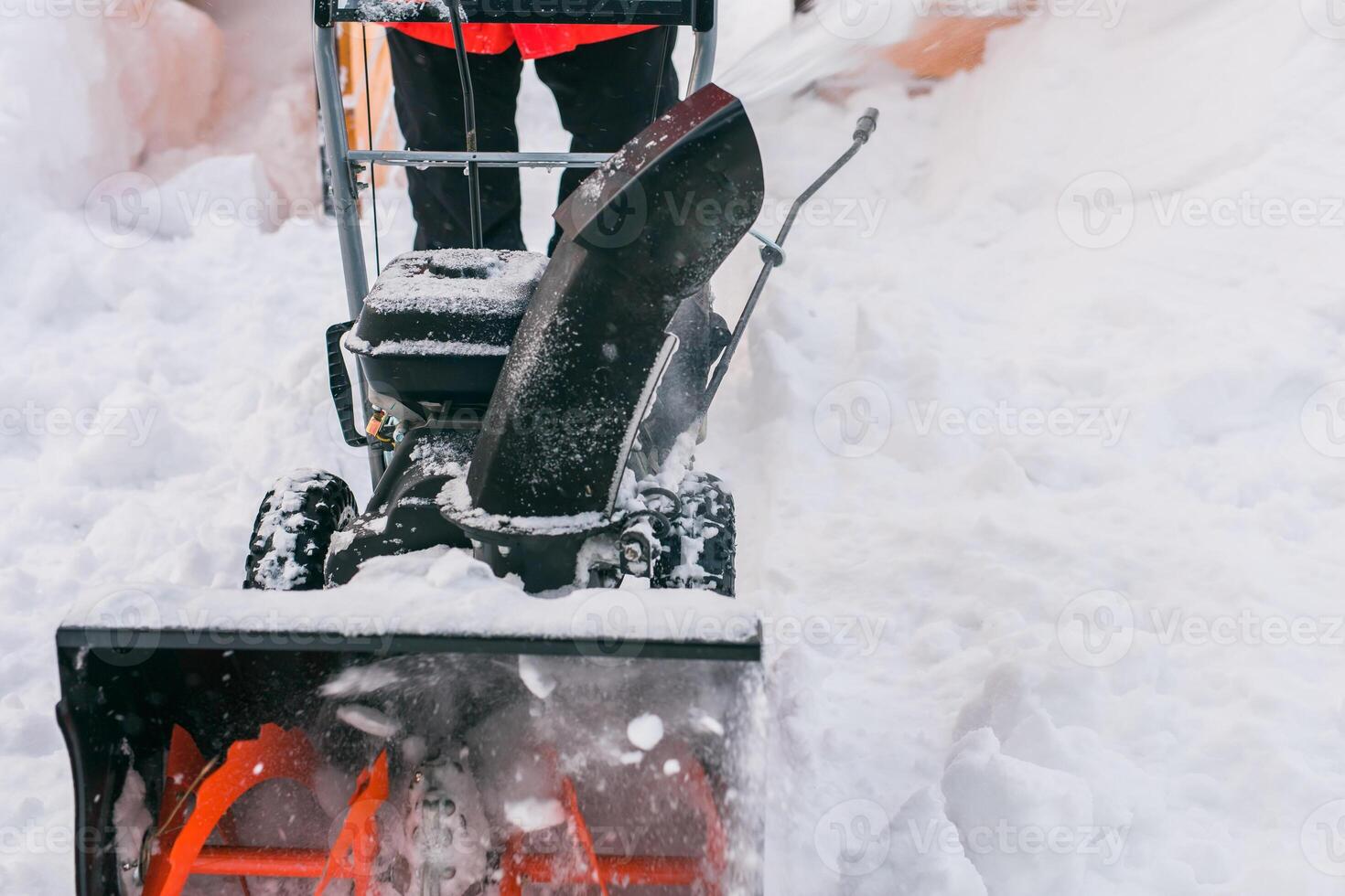 Closeup of red snow blower in action. Senior mature man outdoor in front of house using snowblower machine for removing snow on yard. Snow thrower in winter outside home. Young worker guy blowing snow photo