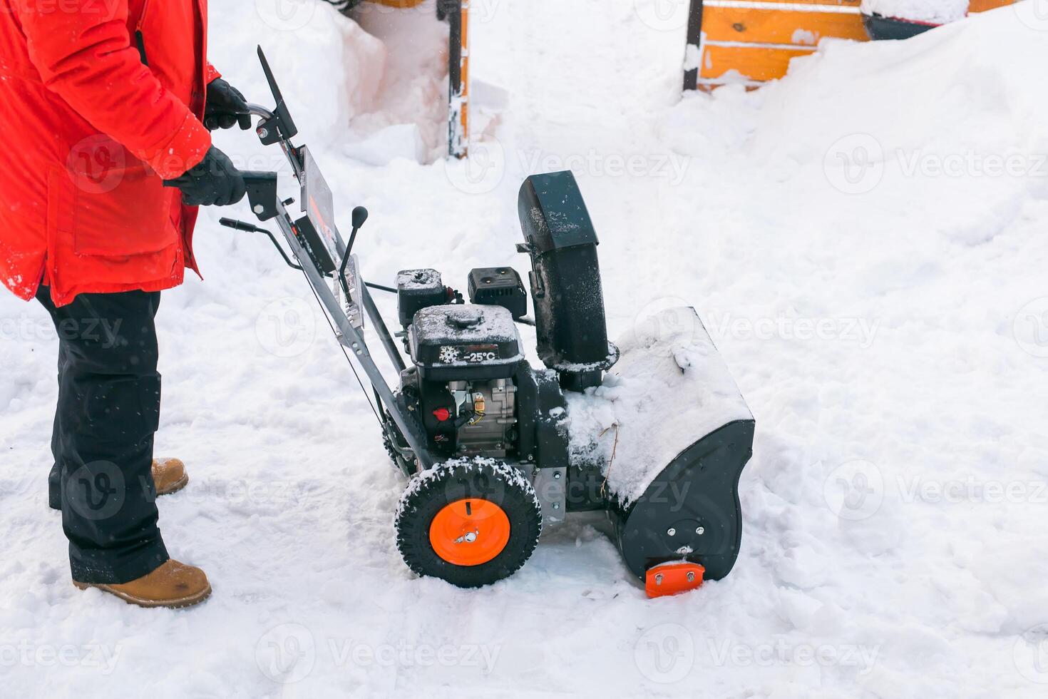 Closeup of red snow blower in action. Senior mature man outdoor in front of house using snowblower machine for removing snow on yard. Snow thrower in winter outside home. Young worker guy blowing snow photo