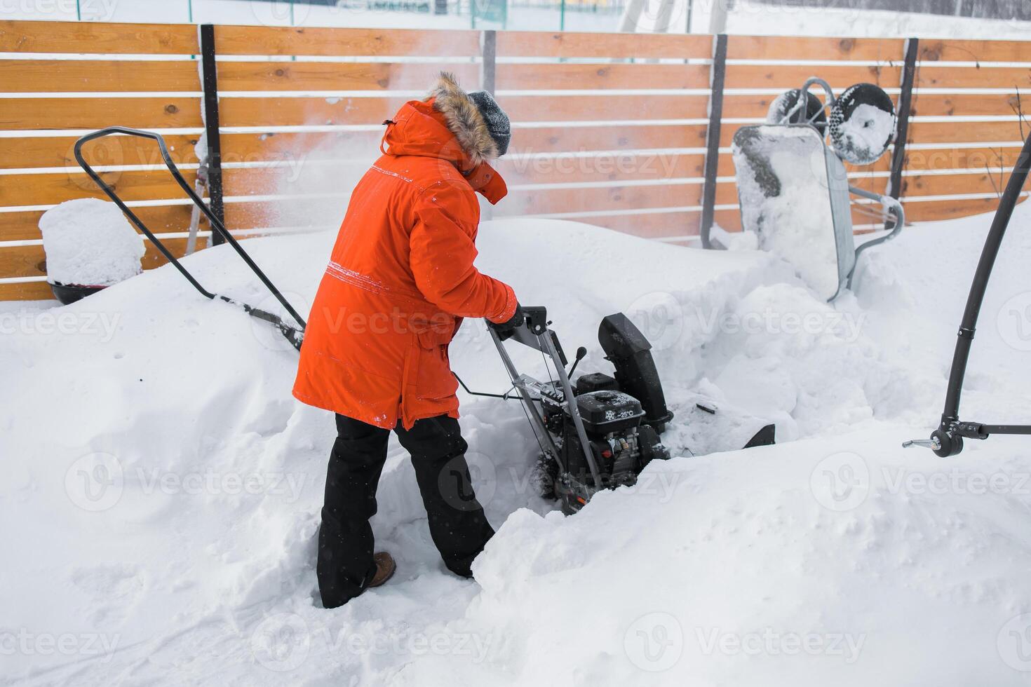 Red snow blower in action. Man outdoor in front of house using snowblower machine for removing snow on yard. Snow thrower in winter outside home. Young worker guy blowing snow photo