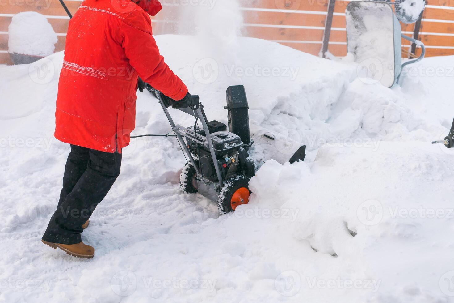 Closeup of red snow blower in action. Senior mature man outdoor in front of house using snowblower machine for removing snow on yard. Snow thrower in winter outside home. Young worker guy blowing snow photo
