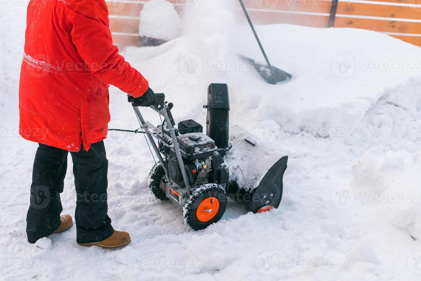 Closeup of red snow blower in action. Senior mature man outdoor in front of house using snowblower machine for removing snow on yard. Snow thrower in winter outside home. Young worker guy blowing snow photo