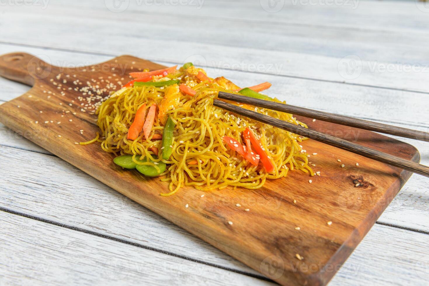 A wooden cutting board with noodles and vegetables photo