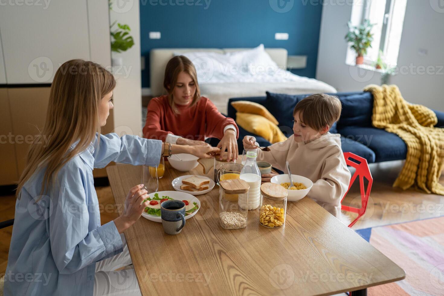 Pleased kid boy holds spoon cocoa while mom and teen sister want drink coffee. Family breakfast time photo