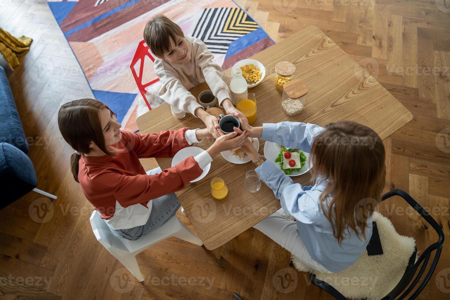 Happy family of three mother and two kids holding one cup of tea while eating breakfast together photo