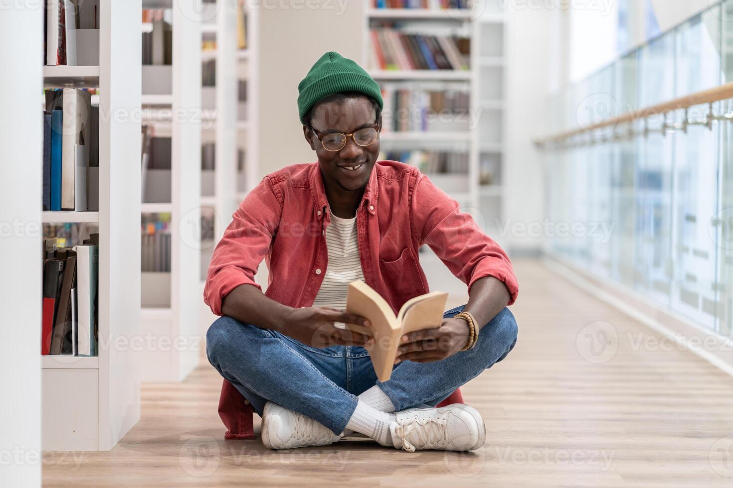 Happy African American millennial guy sitting on floor reading book while visiting library photo