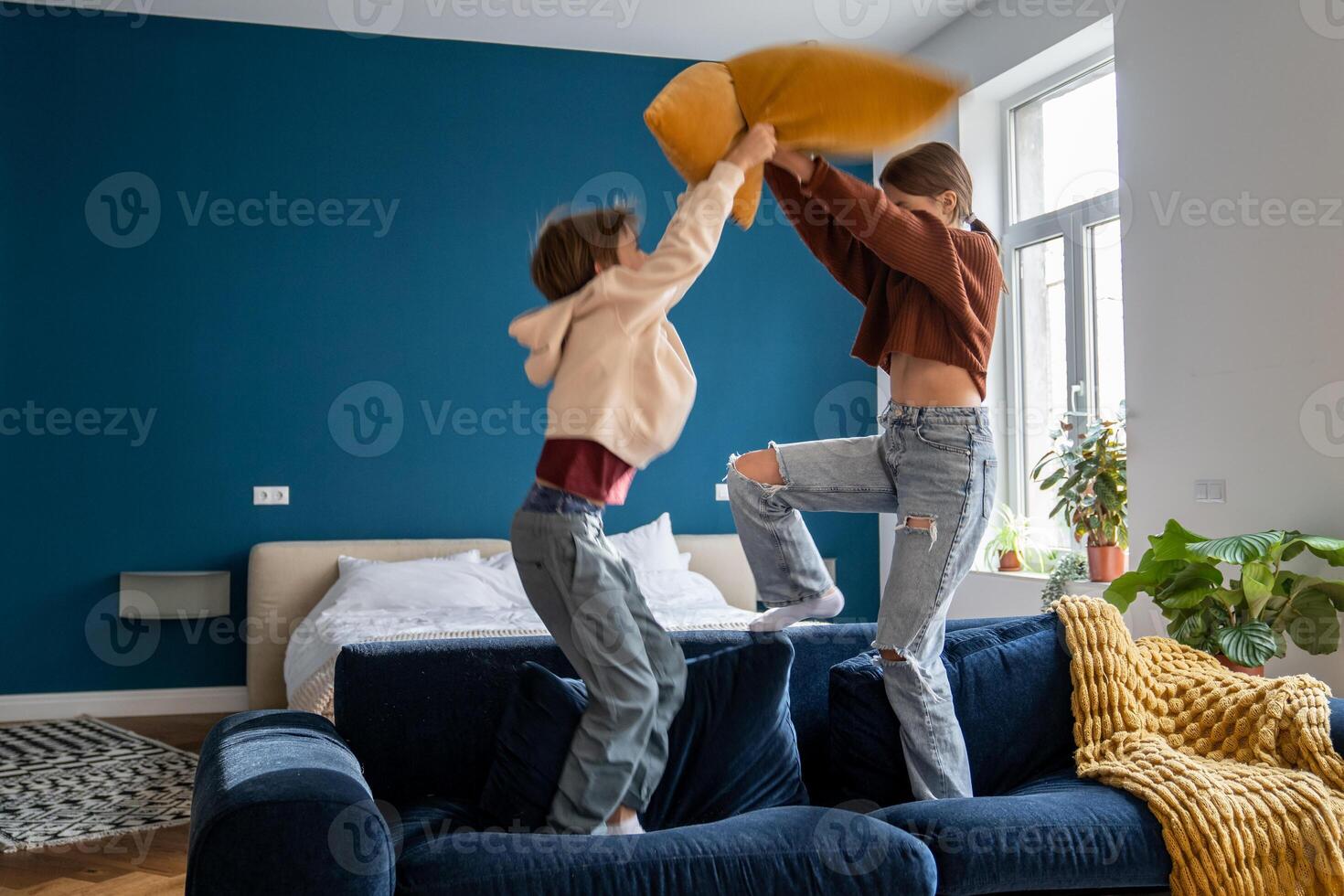 Naughty siblings boy and girl staged pillow fight on couch at home. Fun playing active game together photo