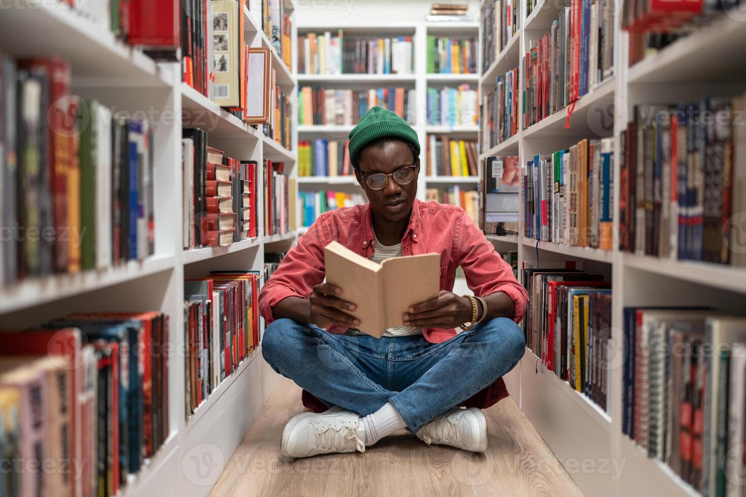 Student african american man reading research textbook in university library sitting on floor. photo