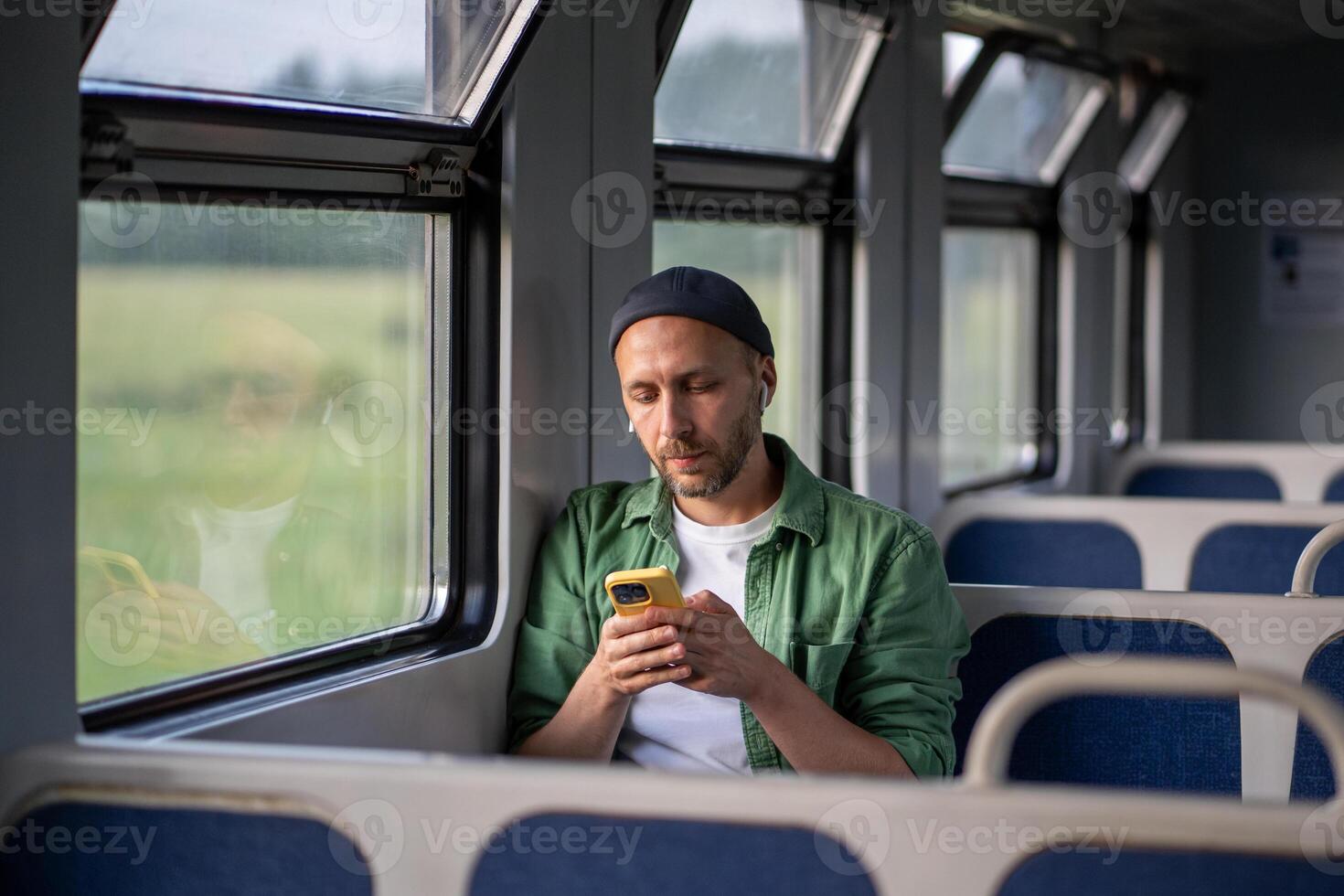 Relaxed man wearing Bluetooth earbuds, using smartphone and surfing Internet, social media in train photo
