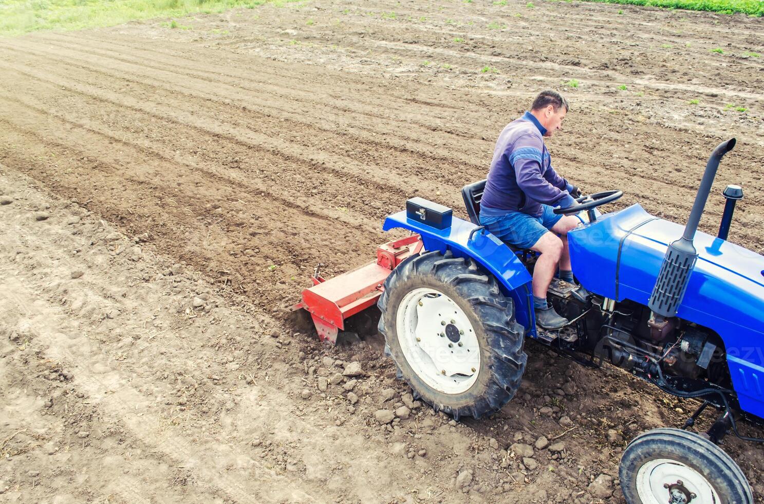 A farmer on a tractor cultivates a farm field. Grinding and loosening soil, removing plants and roots from past harvest. Field preparation for new crop planting. Cultivation equipment. photo