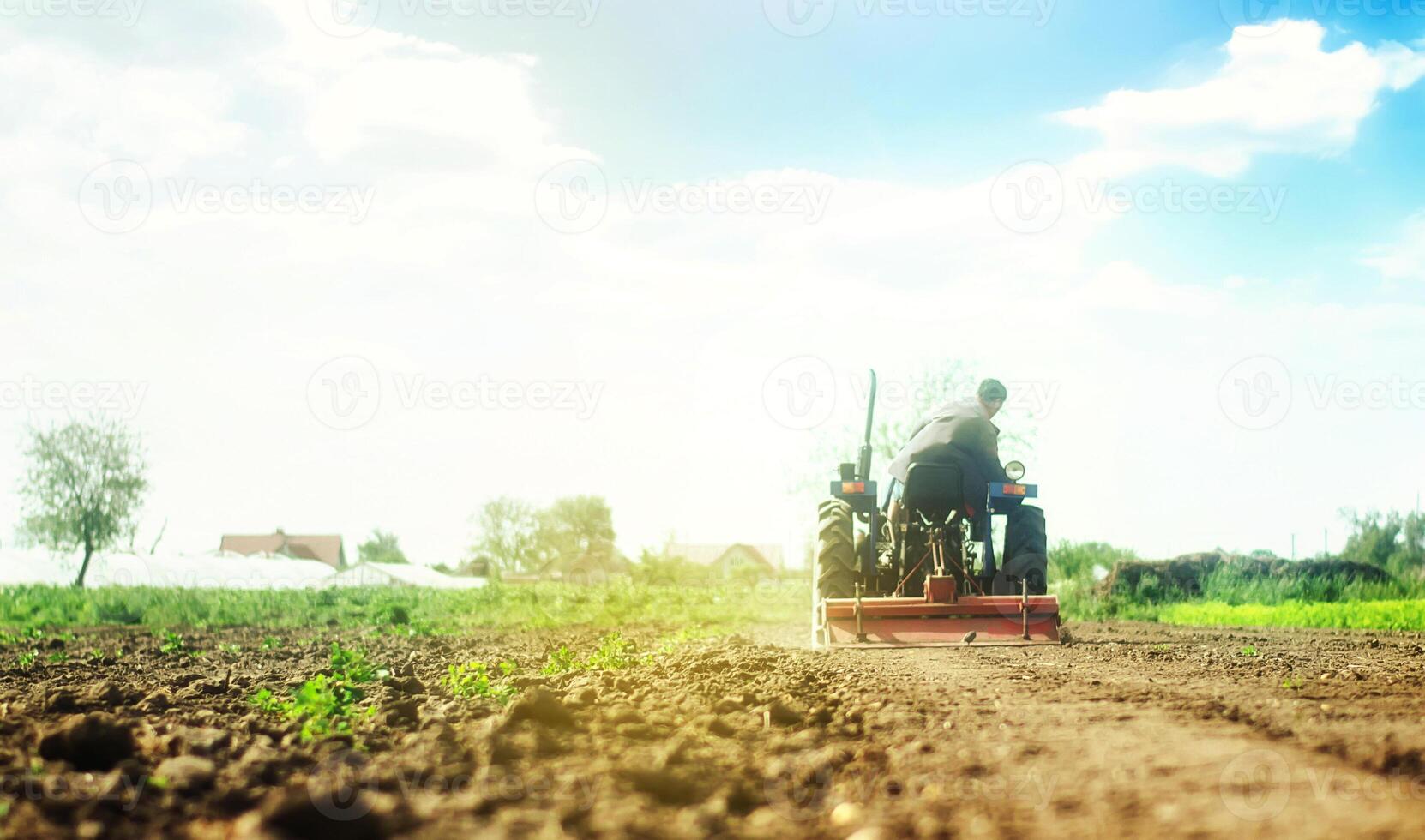 Farmer on a tractor with milling machine loosens, grinds and mixes soil. Loosening the surface, cultivating the land for further planting. photo