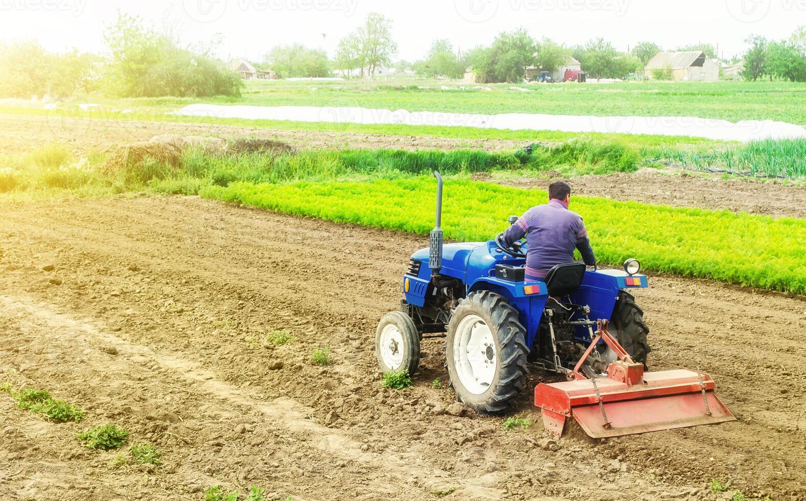 Farmer on a tractor with milling machine loosens, grinds and mixes soil. Loosening the surface, cultivating the land for further planting. Cultivation technology equipment. Farming and agriculture. photo