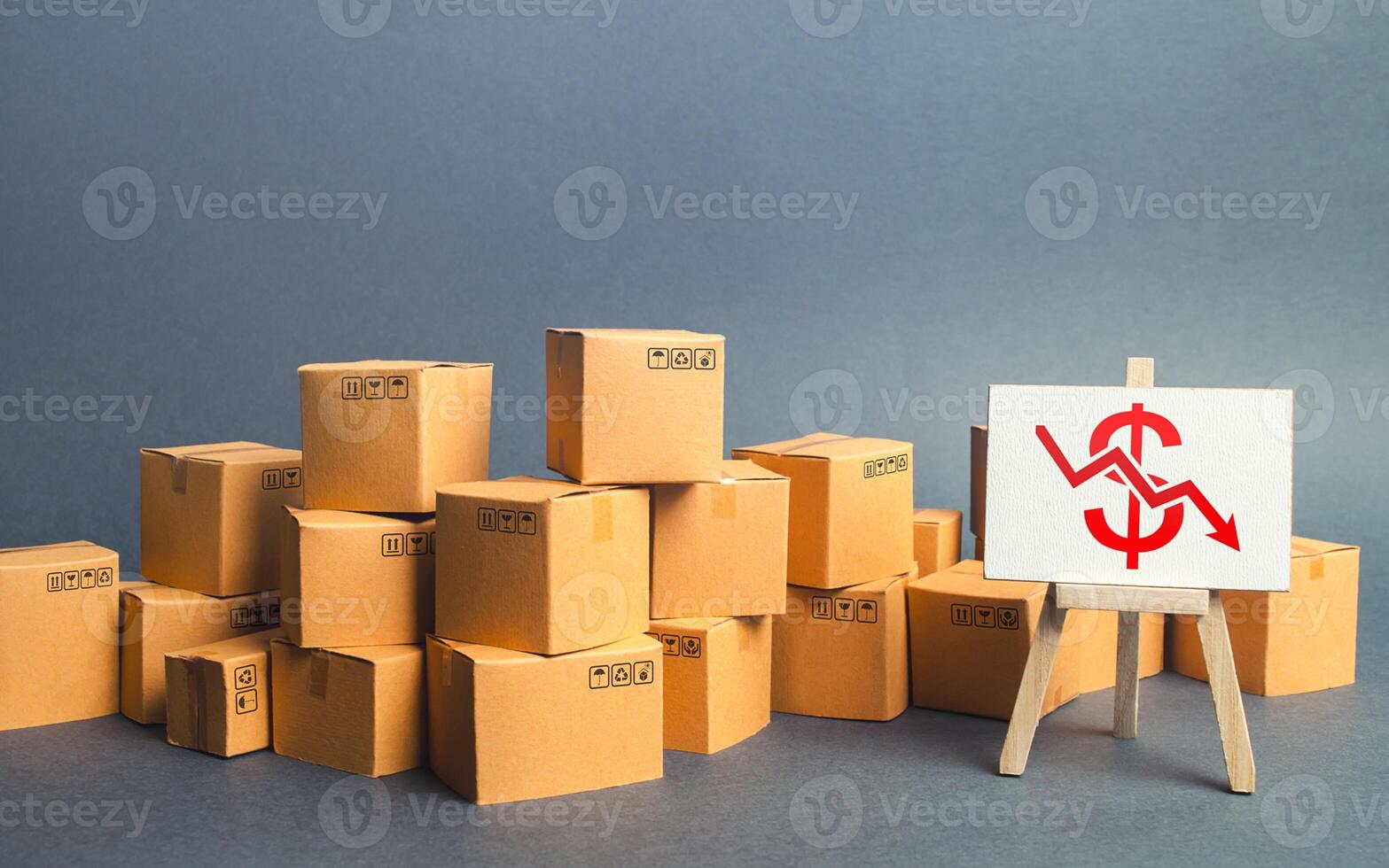Lot of goods cardboard boxes and easel with a red dollar down arrow. Decline trade production rates, decreased sales. Low export. Economic reduced, industry degradation. Marketing, price reduction. photo