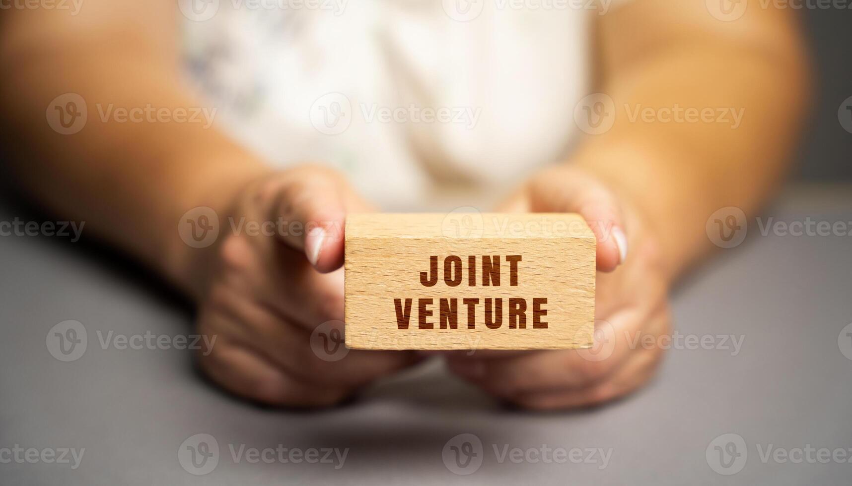 Joint venture on blocks concept. JV is a business entity created by two who parties shared returns and risks and shared governance. Wooden blocks in female hands photo