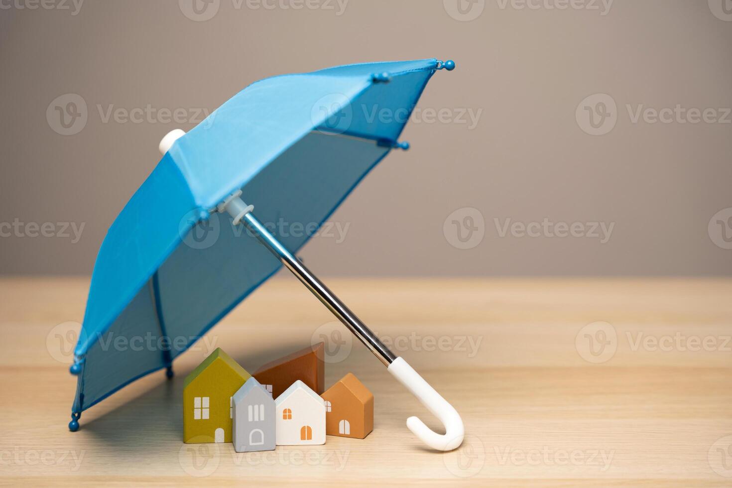 Property and home insurance concept. Wooden houses stand under a blue umbrella. Financial security. Repairs or rebuilding in the event of a covered loss. photo