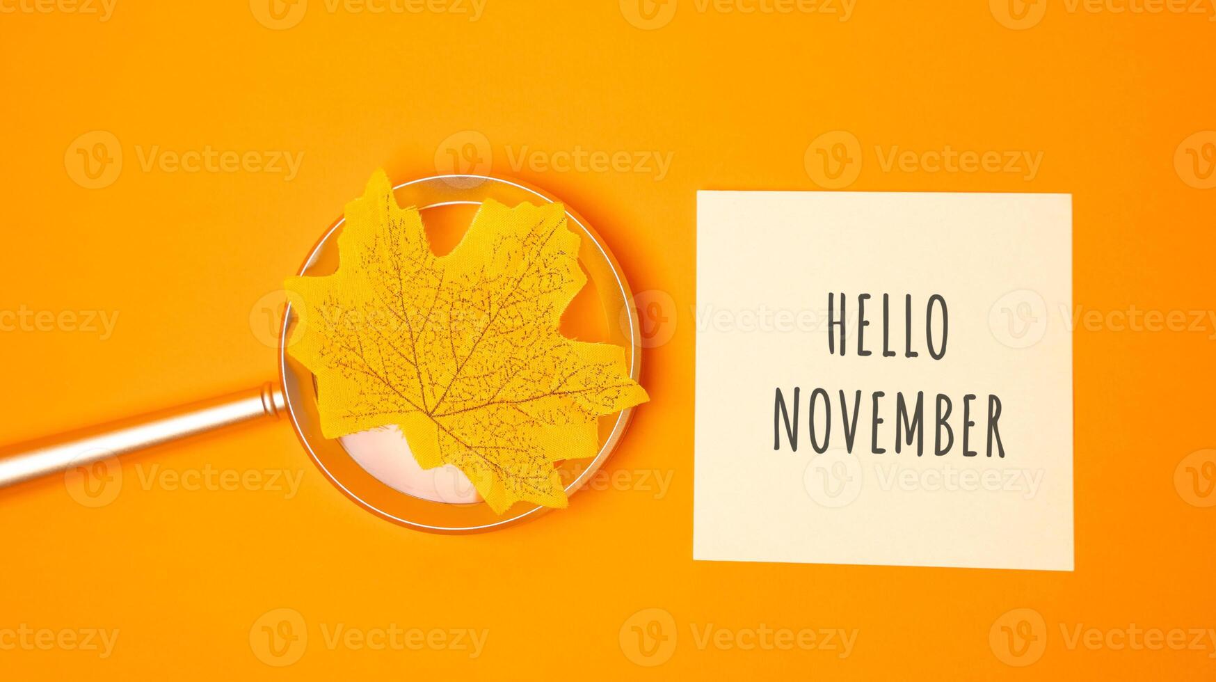 Magnifying glass with yellow leaf and note with words Hello november. Concept of beginning of autumn and new season photo