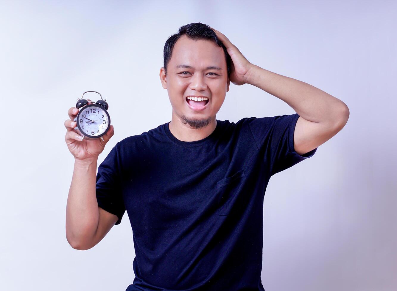 An asian man joyfully holds an alarm clock, celebrating timely moments with a big smile isolated on white background photo