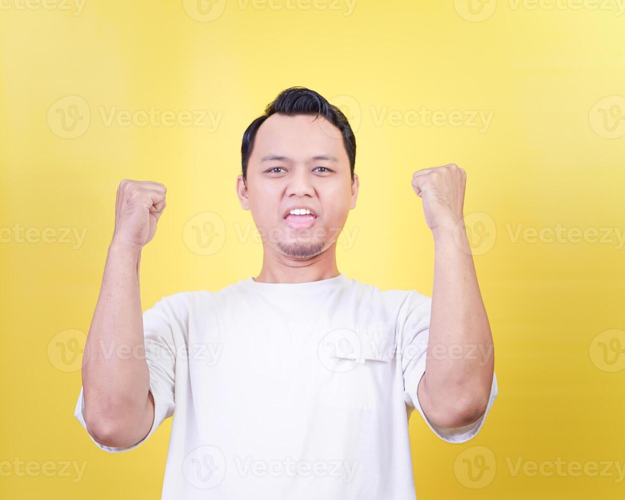 An asian man showing excitement with raised fists against a vibrant yellow background photo