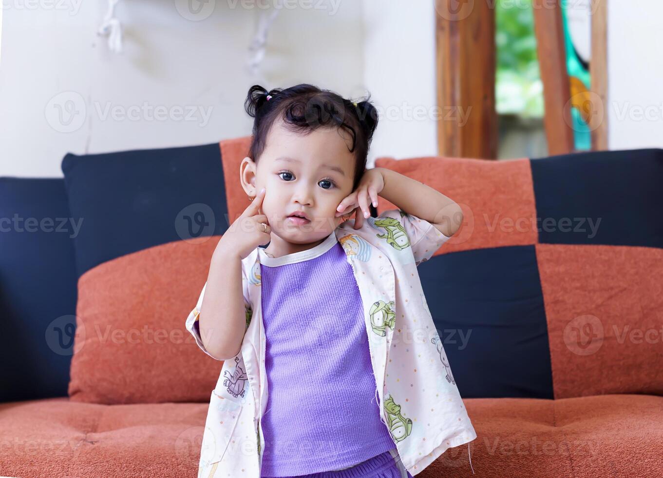 A cute asian child poses playfully in a colorful outfit, sitting on a cozy sofa. photo
