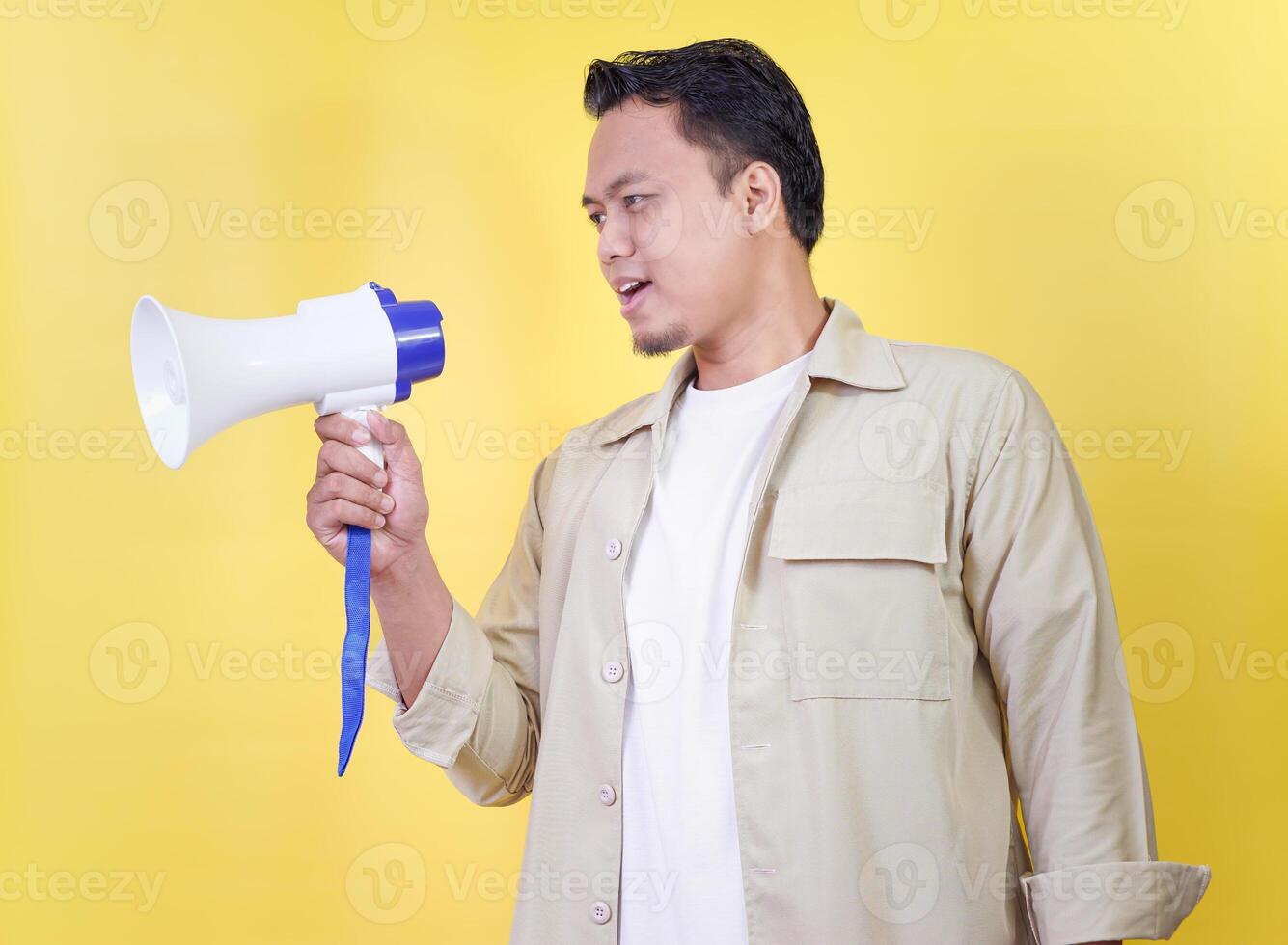 An asian man holds a megaphone, ready to communicate, set against a bright yellow background. photo