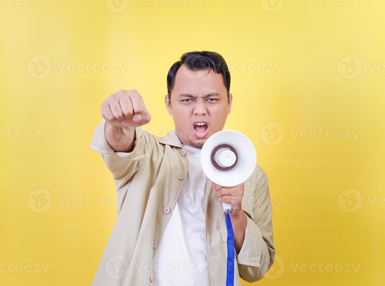 An energetic Asian man makes a fist while holding a megaphone against a bright yellow background photo