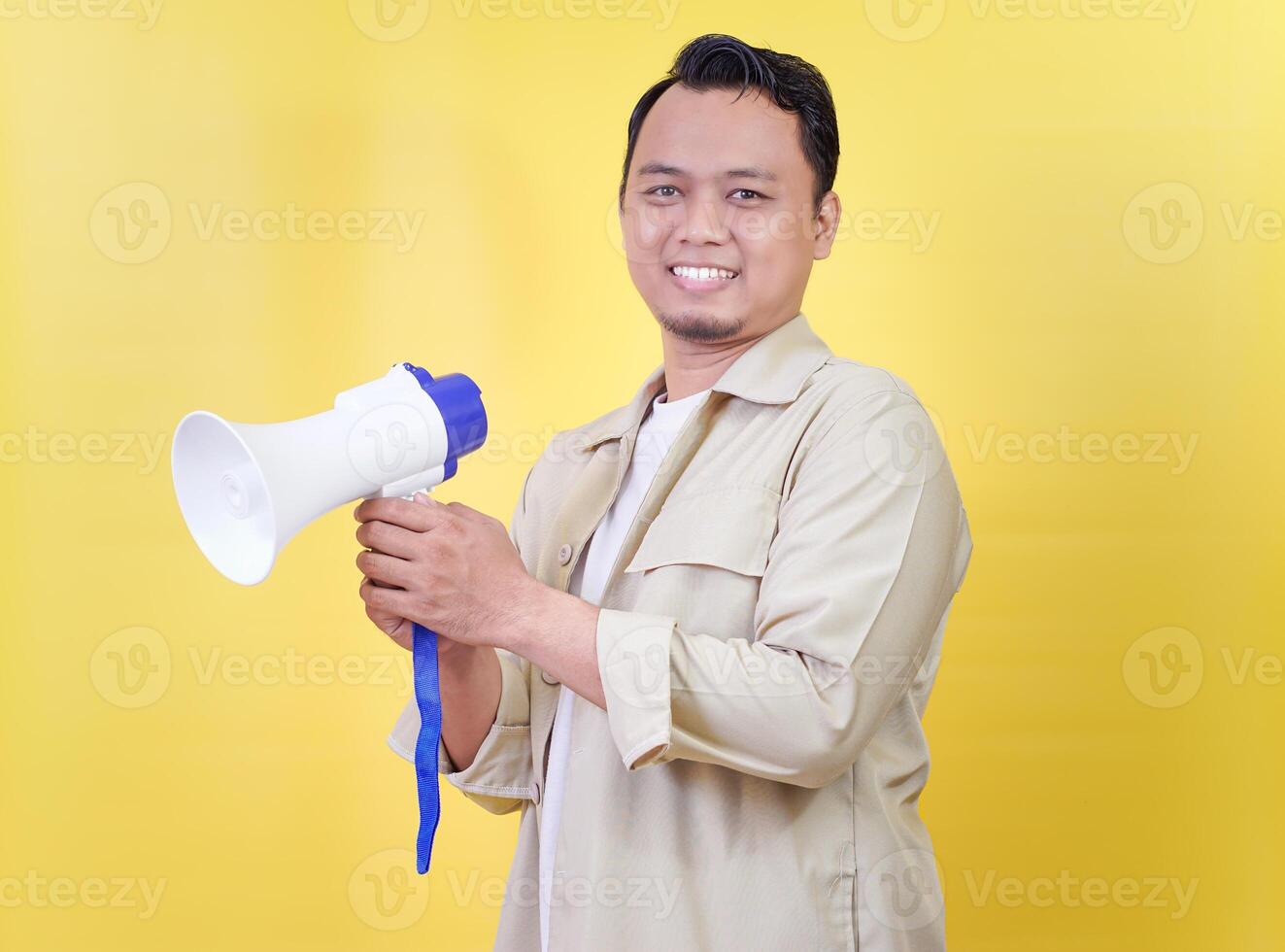 An asian man holds a megaphone, smiling against a bright yellow background photo