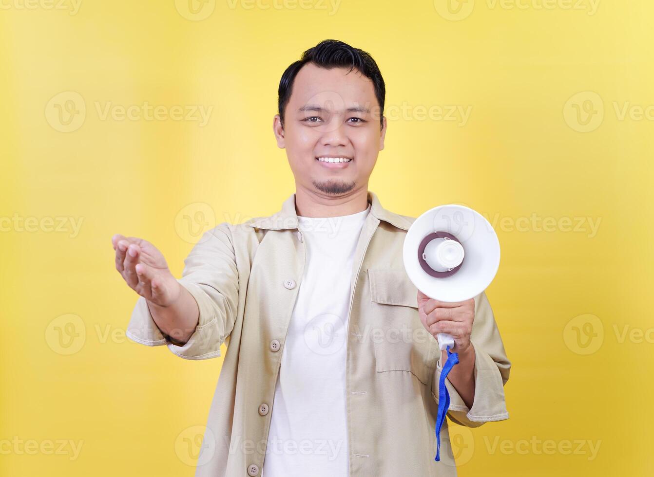 A cheerful asian man holds a megaphone, inviting engagement against a vibrant yellow backdrop. photo