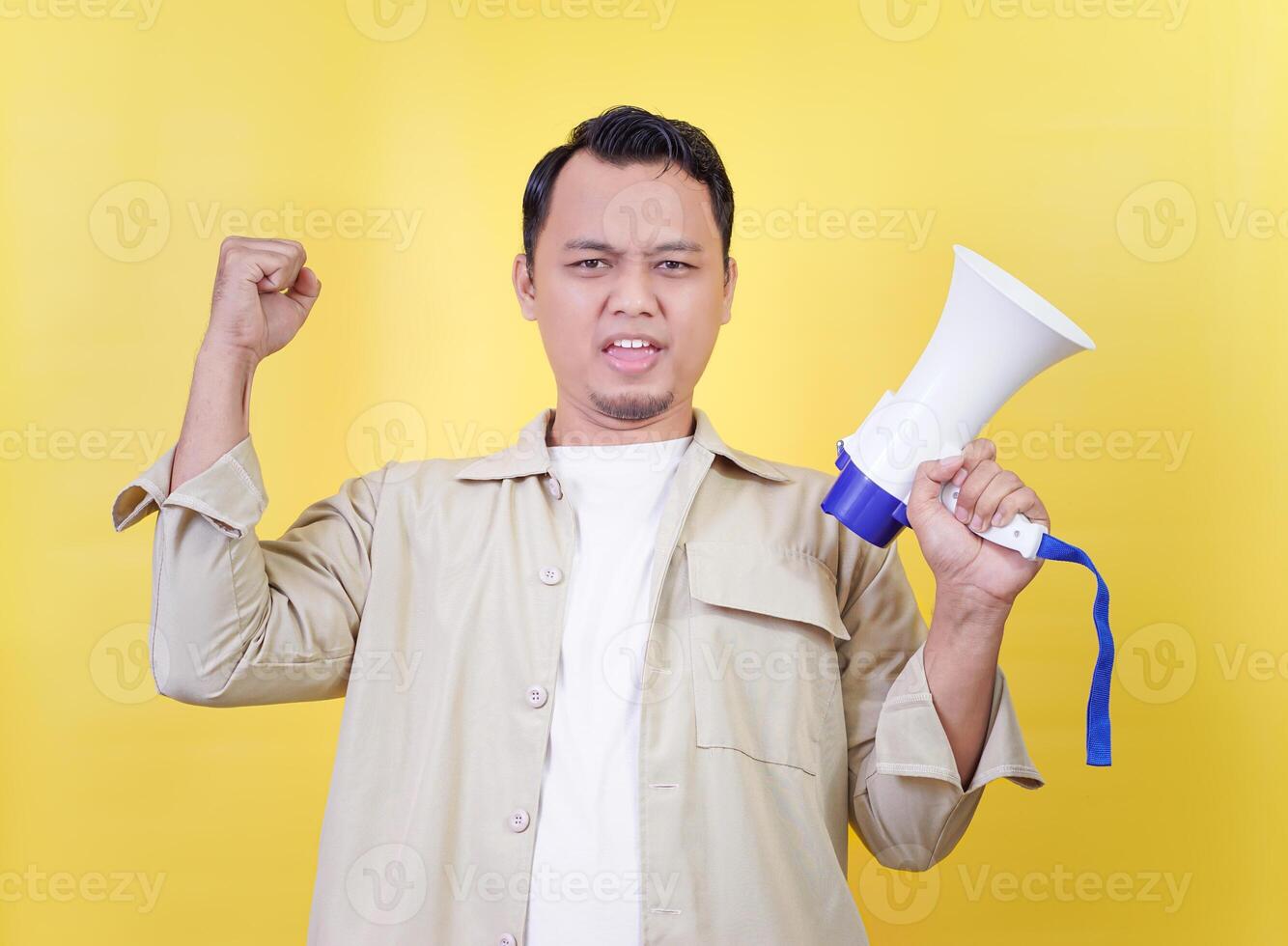 an asian motivated speaker raises a megaphone with determination against a bright yellow backdrop. photo