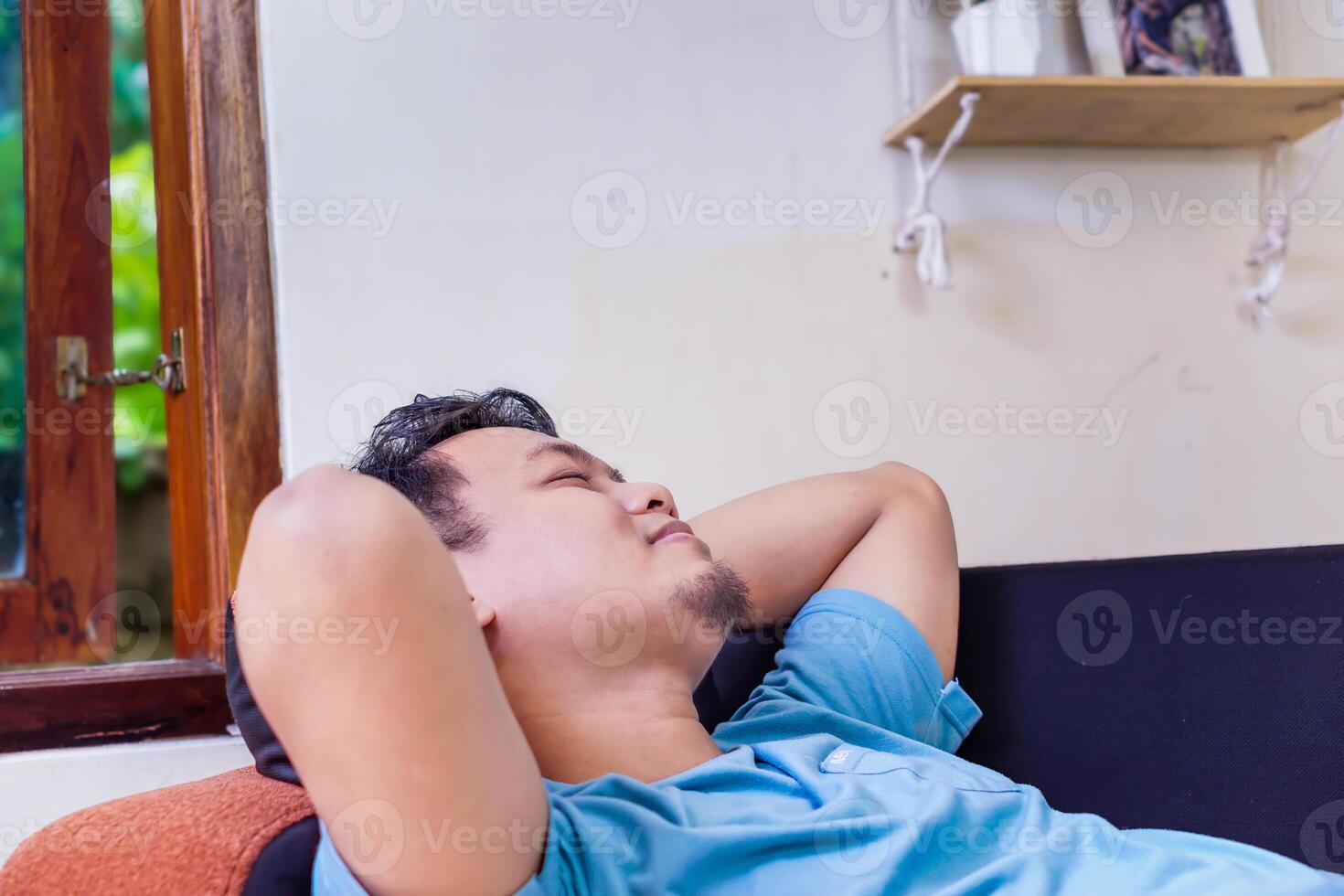 Relaxed man enjoying a peaceful moment at home with eyes closed and arms behind his head photo