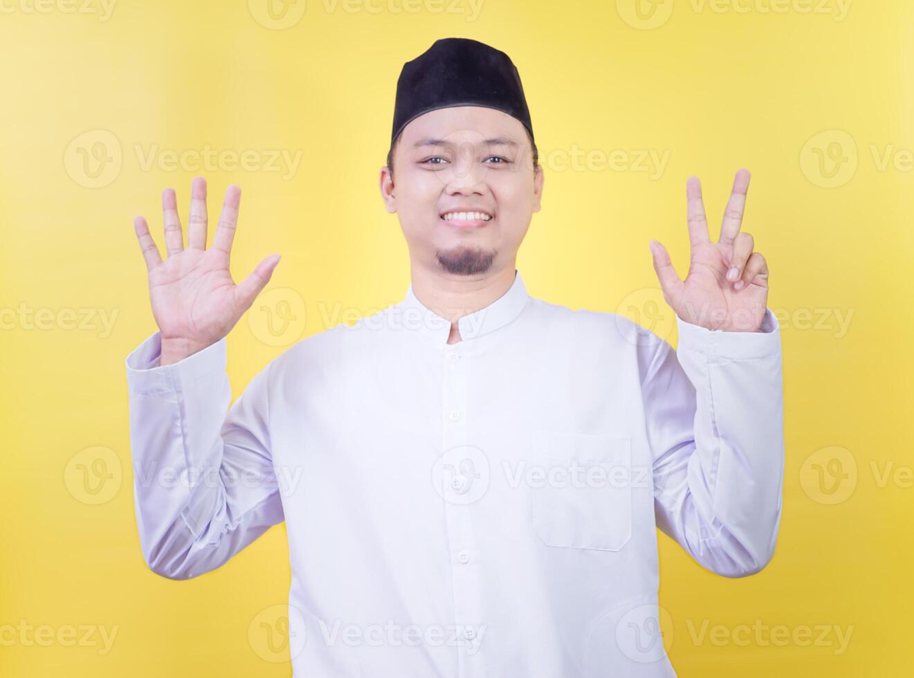 Smiling asian muslim man wearing casual clothes showing and pointing up with fingers number eight photo