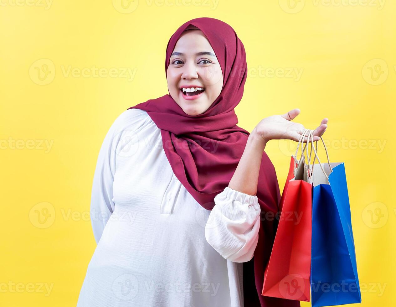 Smiling asian muslim woman in a hijab holding colorful shopping bags against a bright yellow background photo