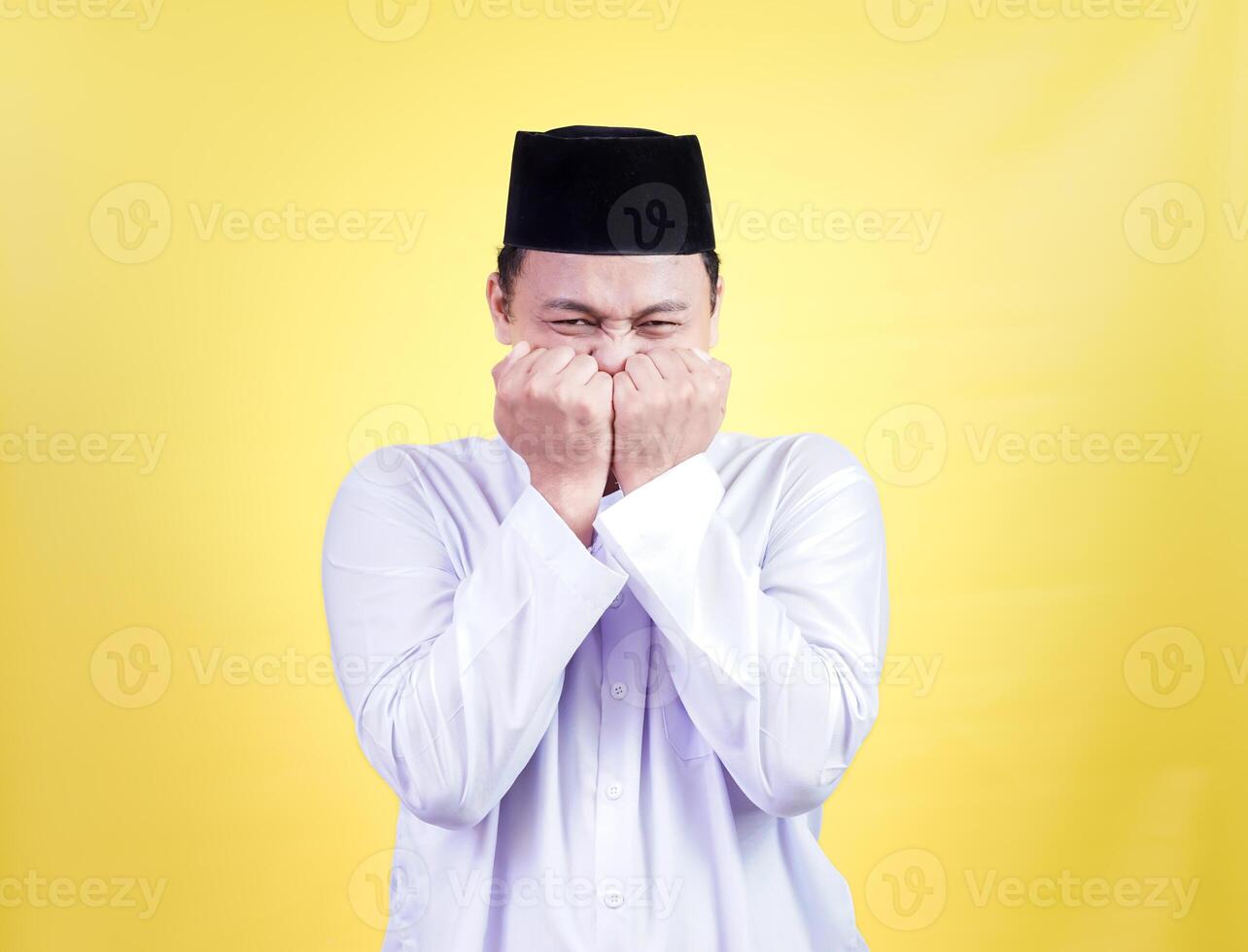 An asian muslim man in traditional attire shows a mix of joy and surprise against a yellow backdrop photo
