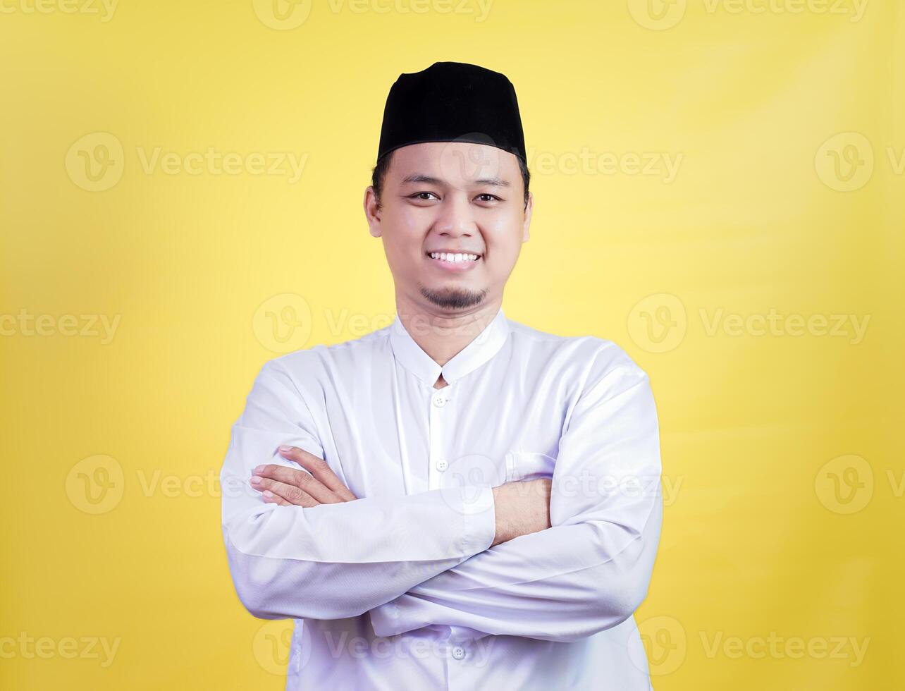 A smiling asian muslim man in a white outfit poses confidently against a yellow background photo