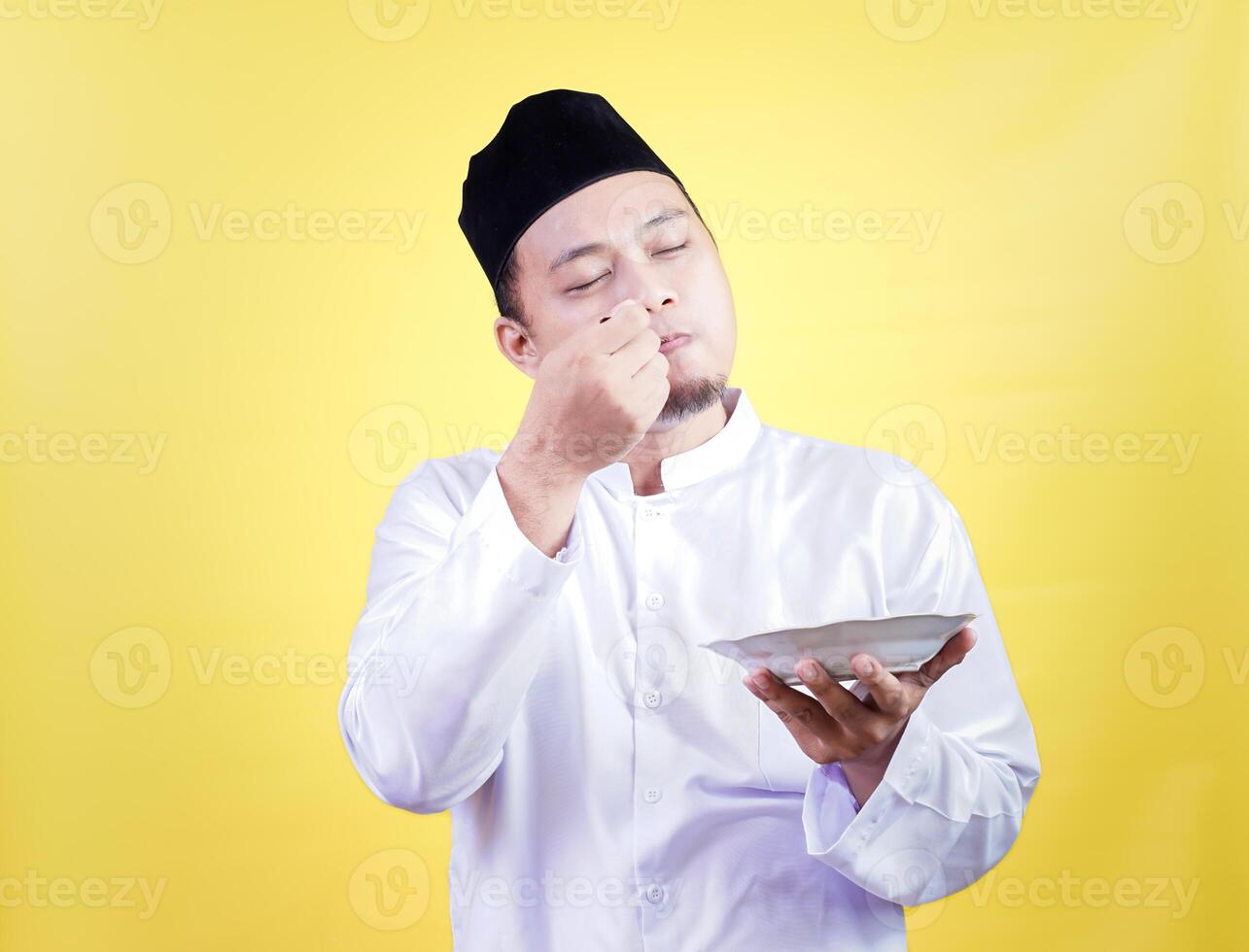 An asian man in traditional attire enjoys tasty food with a satisfied expression against a yellow background photo