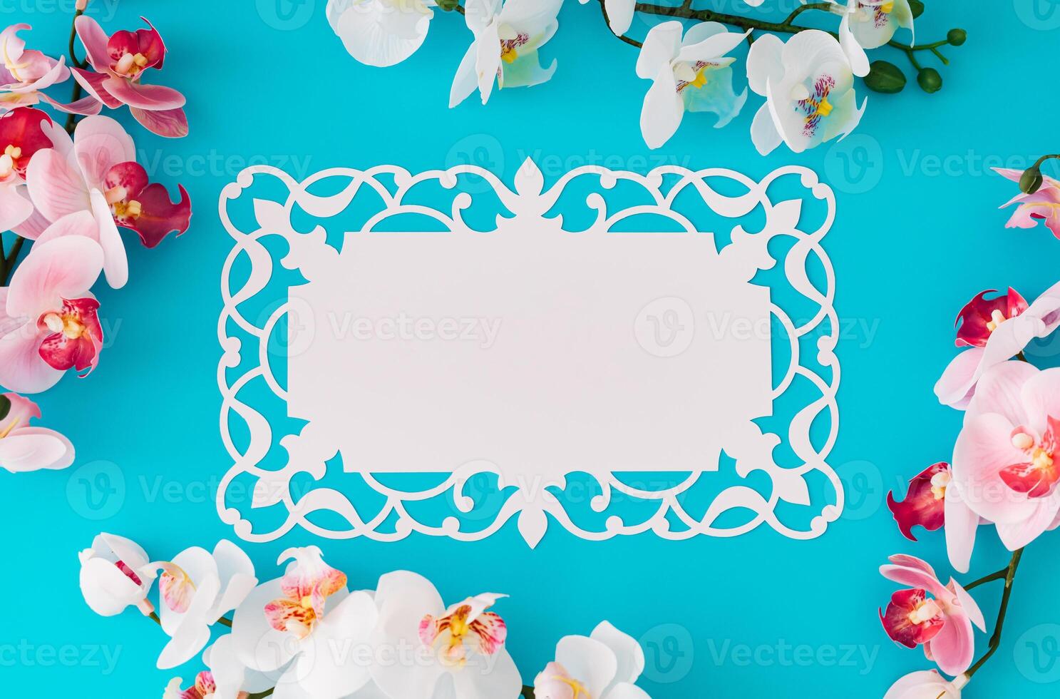Beautiful orchid flowers on light blue background with paper card note. Minimal concept. Creative spring and summer layout. Flower aesthetic with unique copy space. Flat lay, top of view. photo