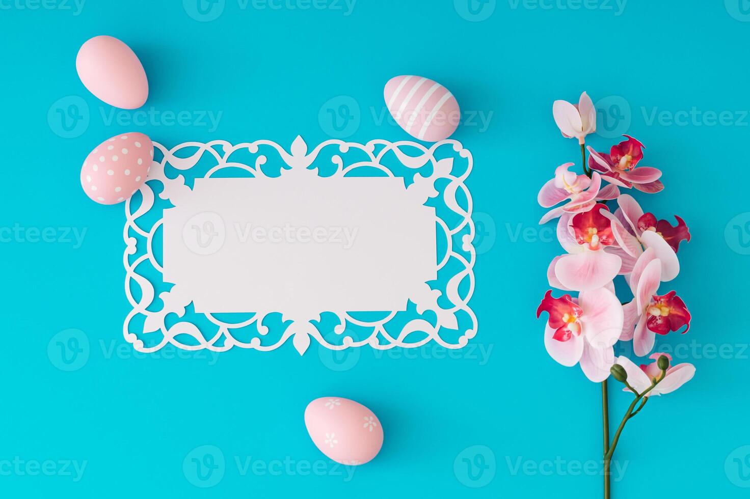 Pink colored eggs and orchid flower on blue background with paper card note. Minimal Easter concept. Creative festive spring holiday layout. Easter aesthetic with unique copy space. Flat lay. photo