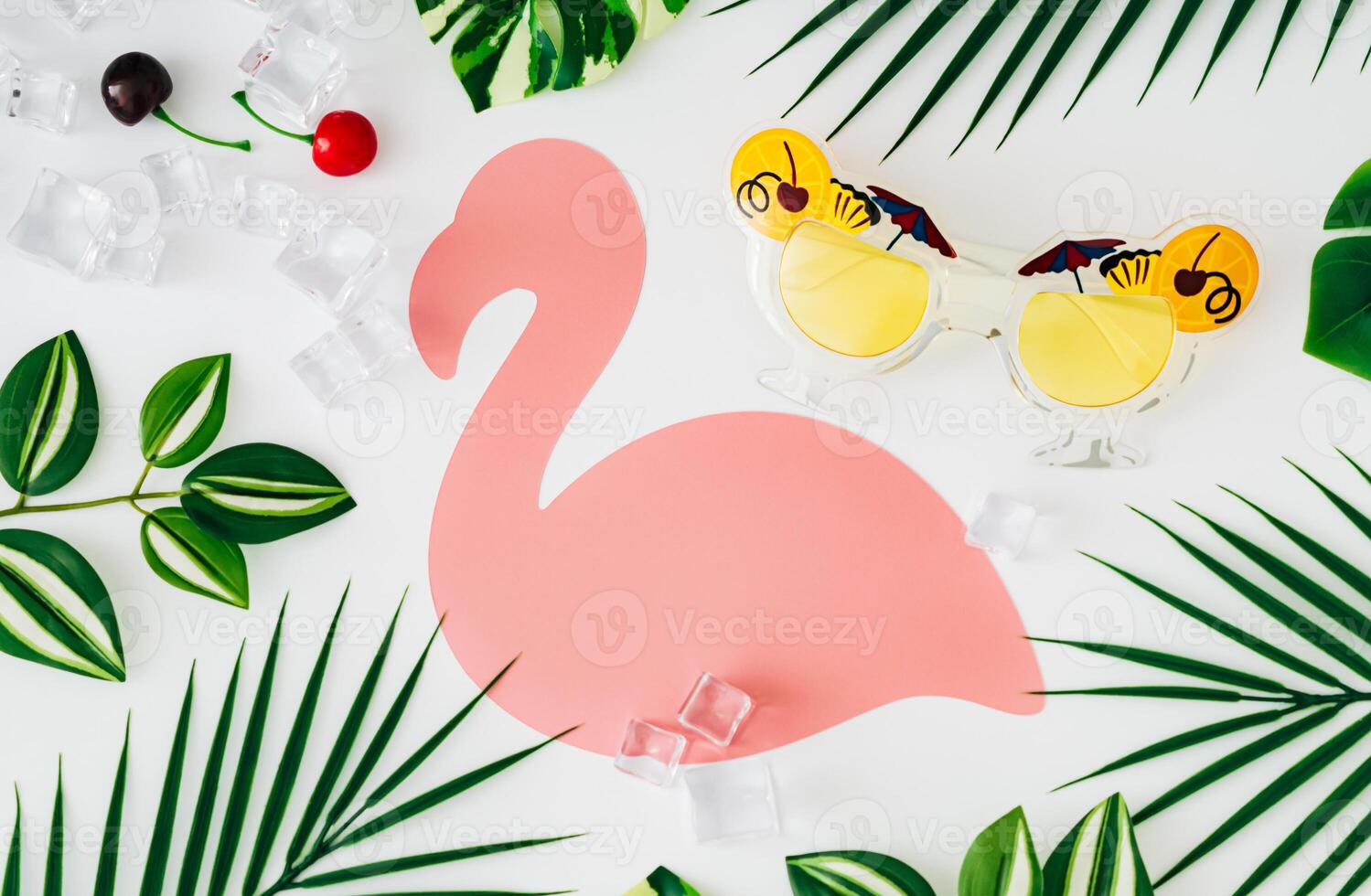 Creative scene with tropical leaves, party sunglasses, ice cubes and red cherries on white background with pink flamingo paper card note. Summer aesthetic concept. Unique copy space. Flat lay. photo