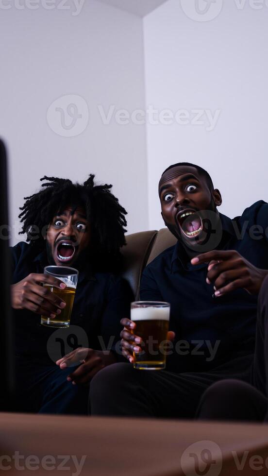 two men watch a screen with amazed expressions while enjoying beverages photo