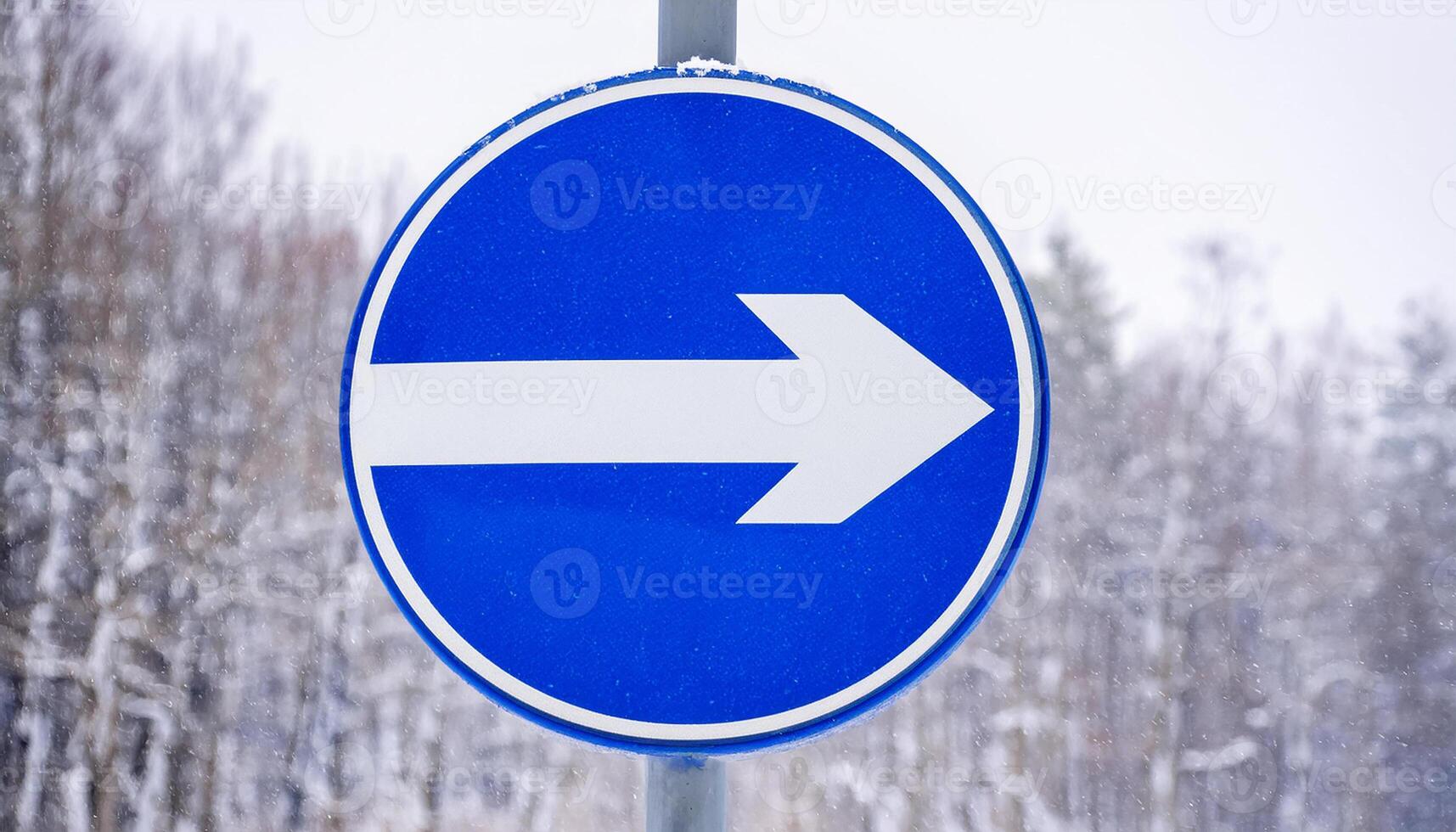 Round blue traffic sign with white arrow. Winter snowy background. photo