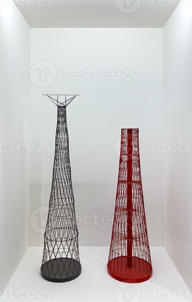 Two detailed scale models of radio towers, one black and one red, exhibited on a white pedestal in a minimalist gallery. The intricate lattice structures emphasize the technical and architectural photo