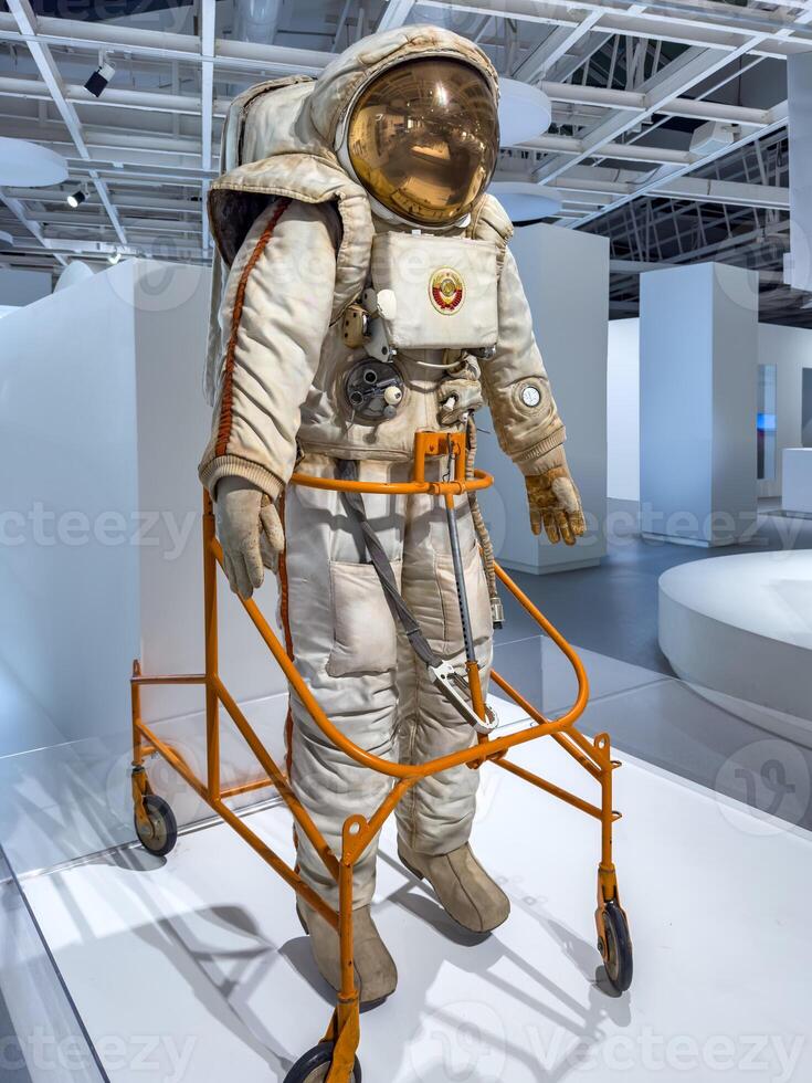 A detailed vintage Soviet-era space suit equipped with life support systems and a reflective visor. The suit features intricate details, including control mechanisms, a chest-mounted unit, and the photo